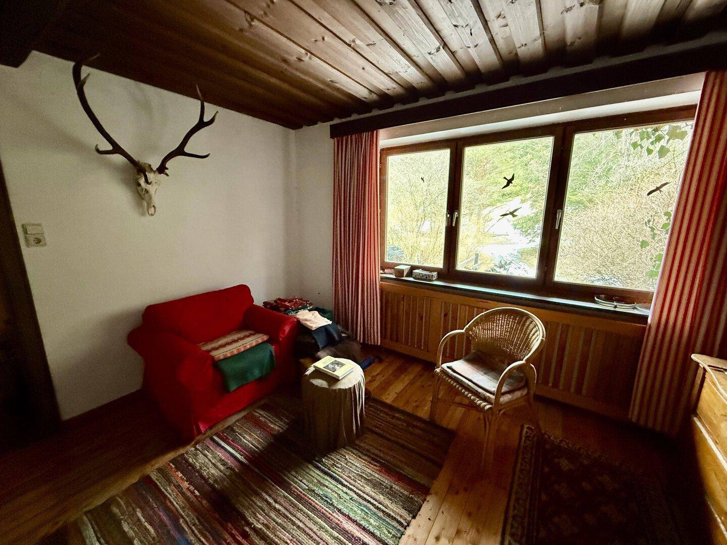 Gemütliches Schlafzimmer mit Holzbalkendecke, rotem Sessel und traditioneller Dekoration.