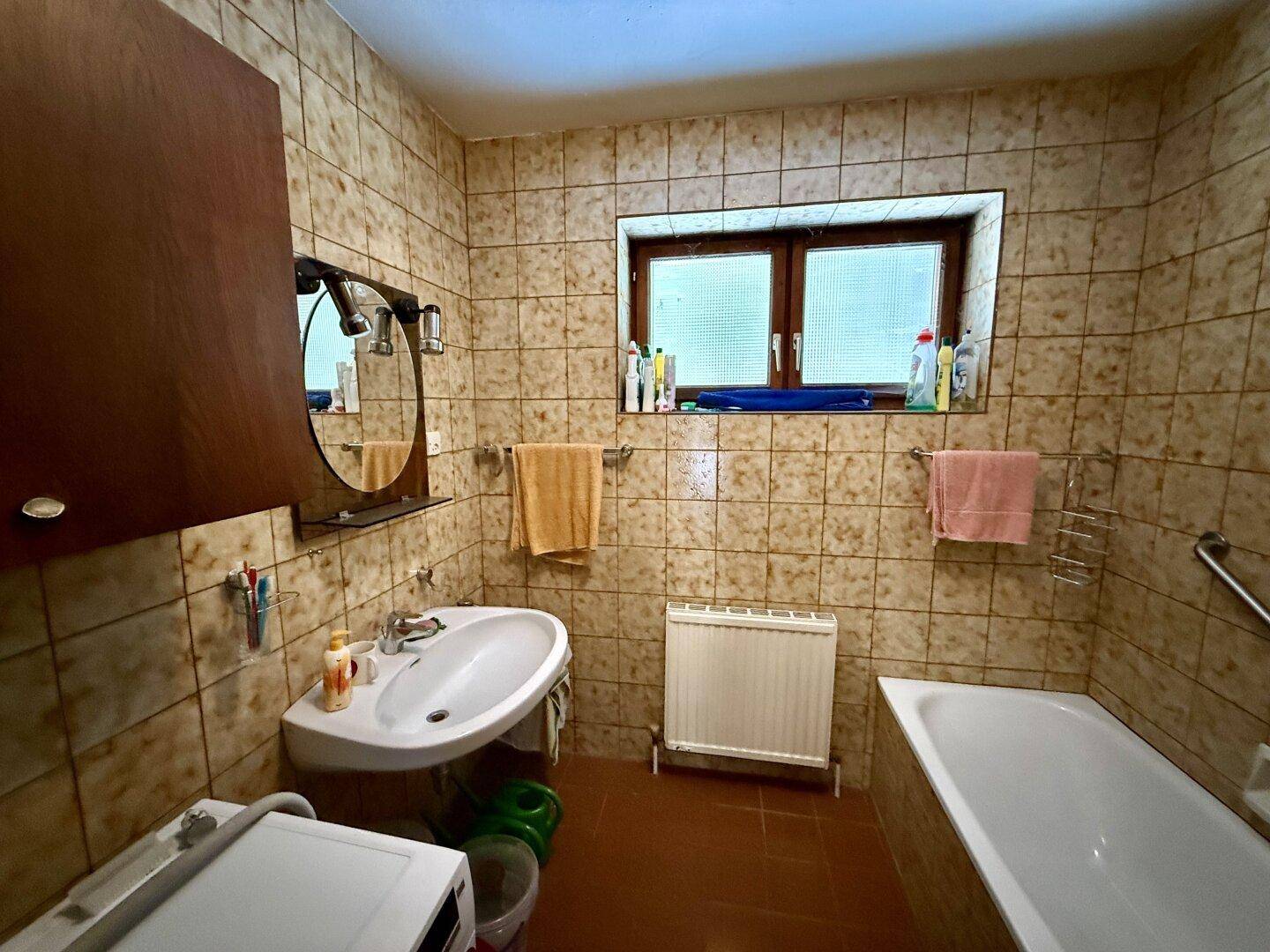 Gefliestes Badezimmer mit Badewanne, Waschbecken und Fenster im traditionellen Stil.