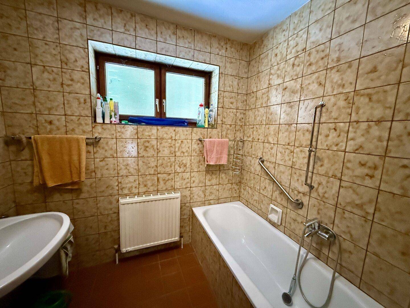 Gefliestes Badezimmer mit Badewanne, Waschbecken und Fenster im traditionellen Stil.