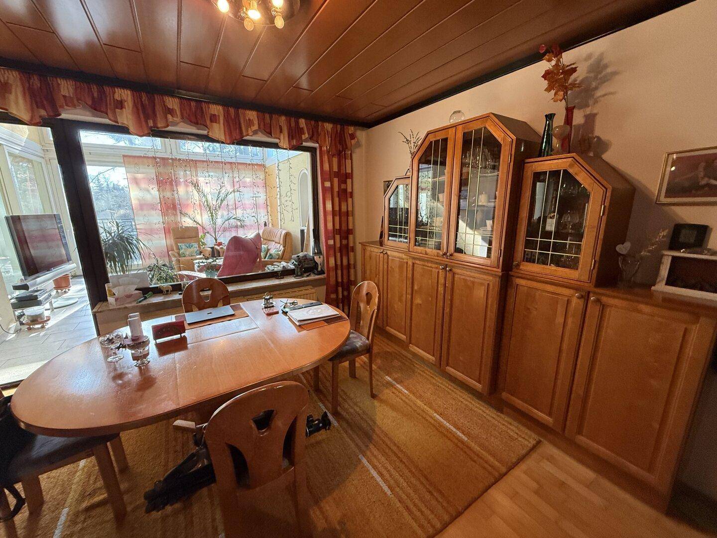Heller Essbereich mit Holzmöbeln und Blick in den angrenzenden Wintergarten.