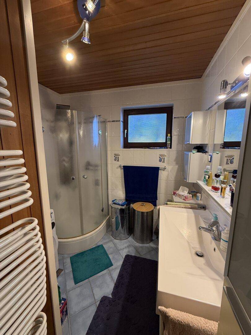 Funktionales Badezimmer mit Duschkabine, Waschbecken und beheiztem Handtuchhalter.