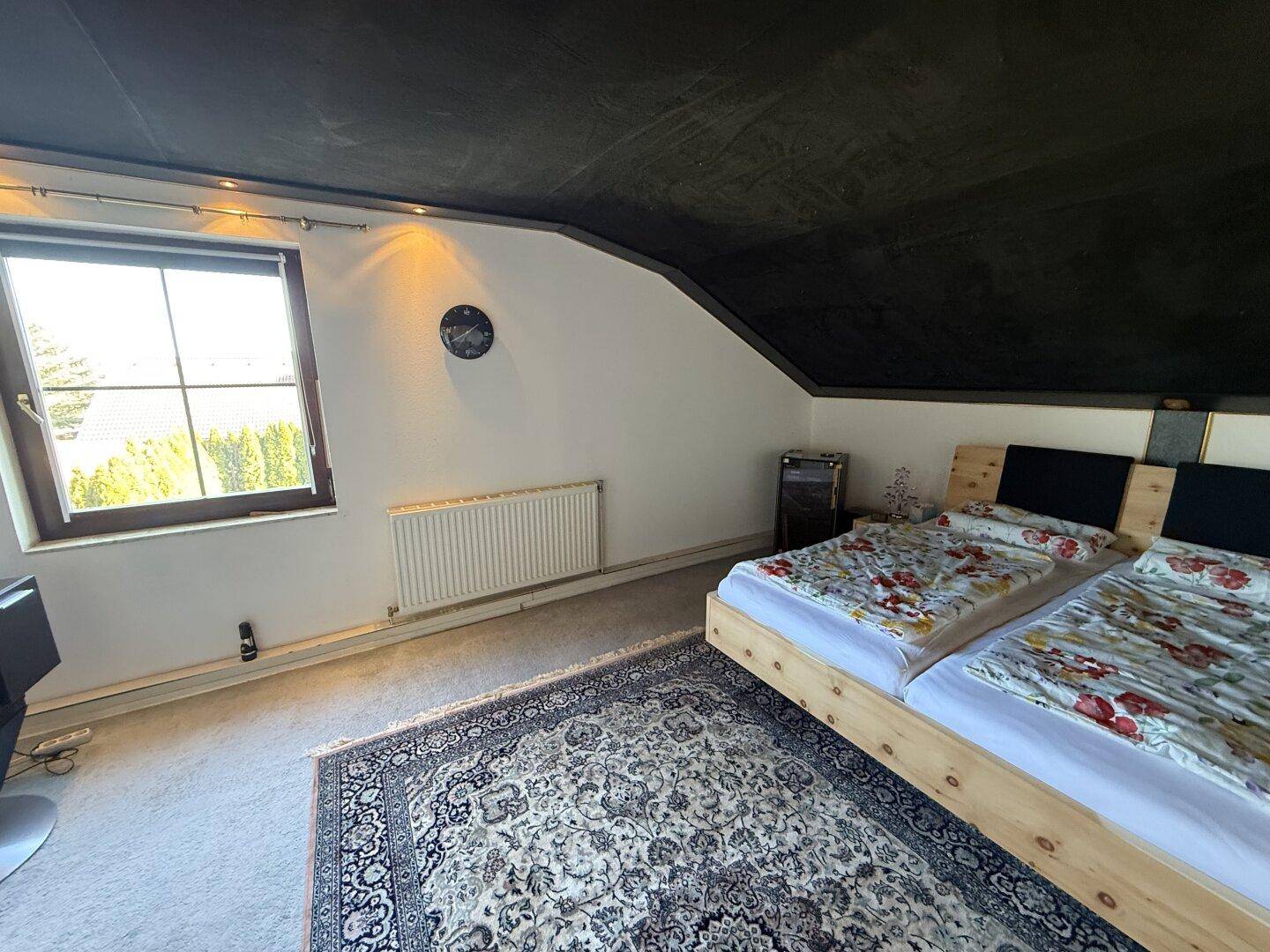 Gemütliches Schlafzimmer im Dachgeschoss mit schrägen Wänden und Teppichboden.