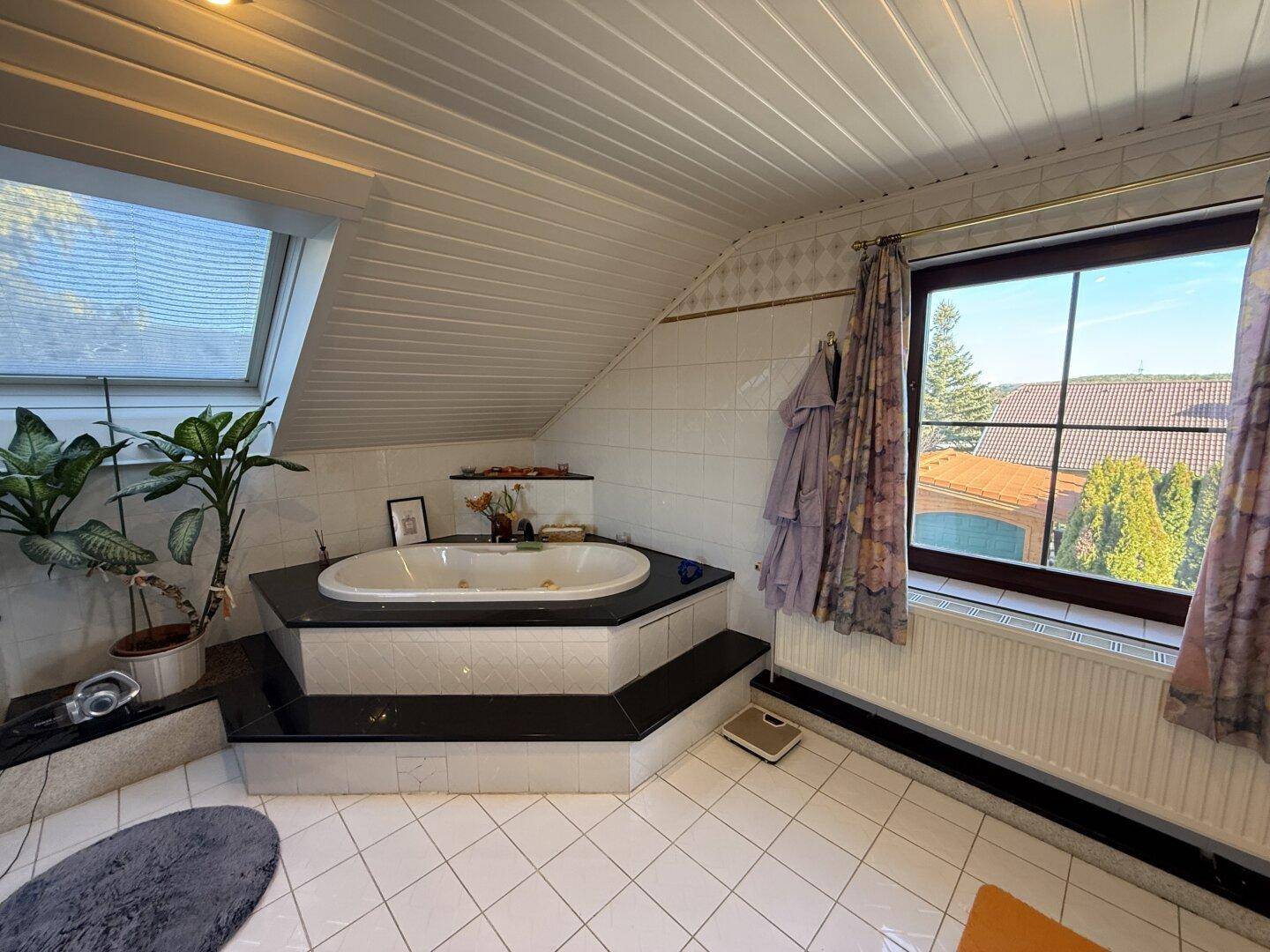 Geräumiges Badezimmer im Dachgeschoss mit Eckbadewanne, Dachfenster und Fliesenboden.