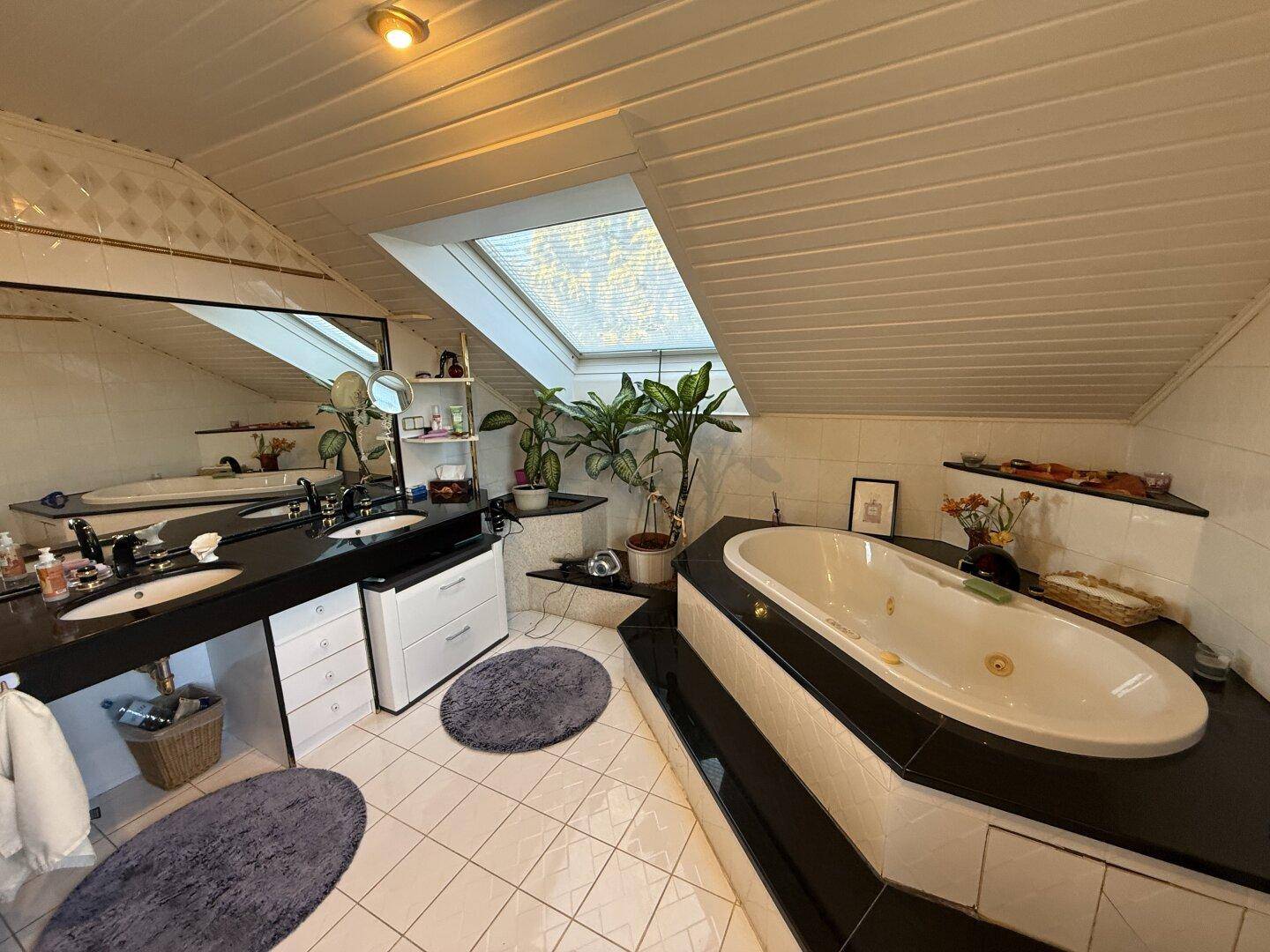Helles Dachgeschoss-Badezimmer mit Eckbadewanne, Doppelwaschbecken und Dachfenster.
