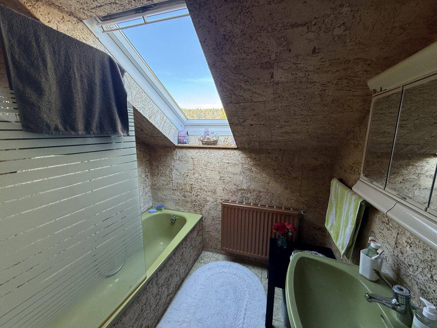 Älteres Badezimmer im Dachgeschoss mit grüner Badewanne, Waschbecken und Dachfenster.
