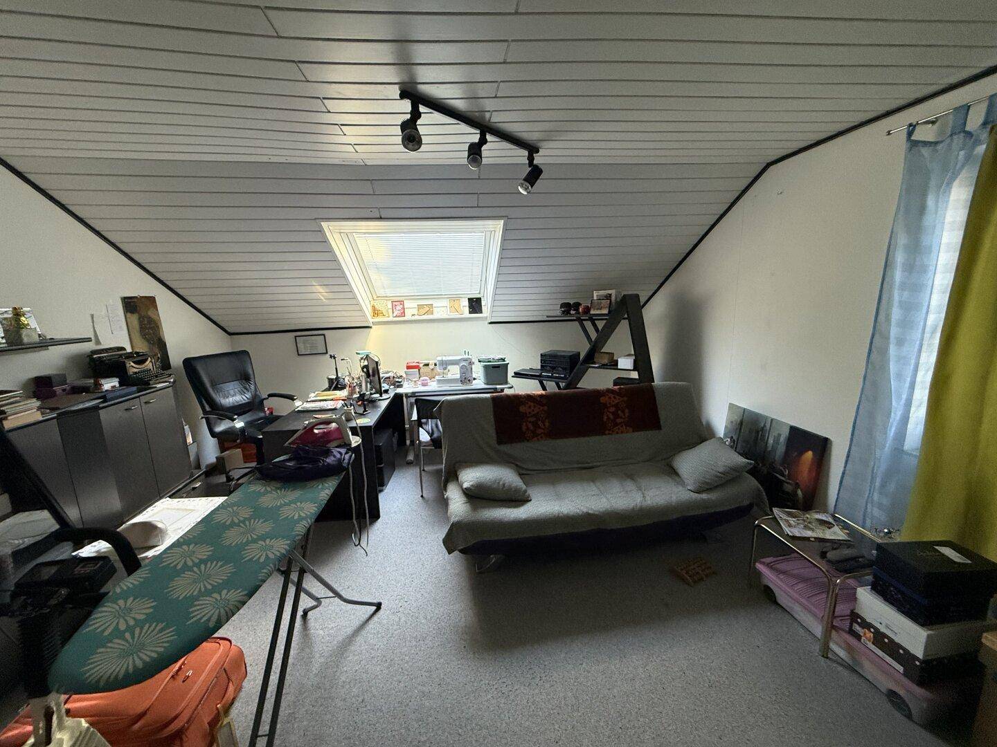 Dachgeschossraum als Büro oder Hobbyraum genutzt mit Schreibtisch und Sofa.