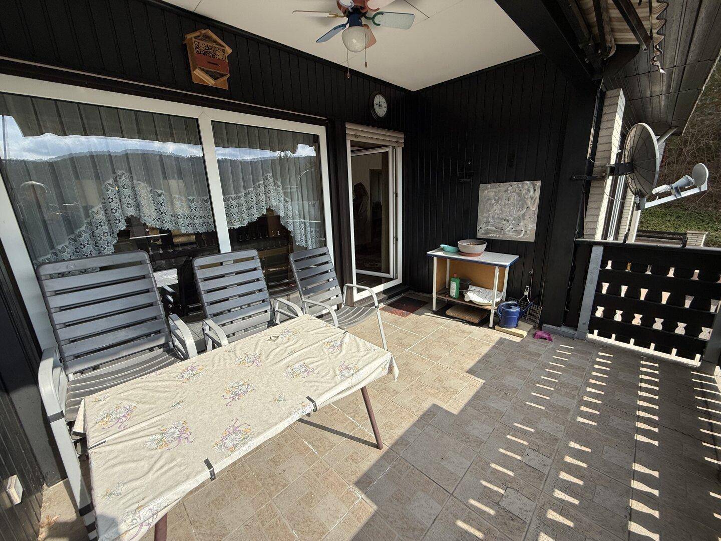 Überdachter Balkon mit Fliesenboden, Sitzgelegenheiten und Deckenventilator, ideal für Entspannung.