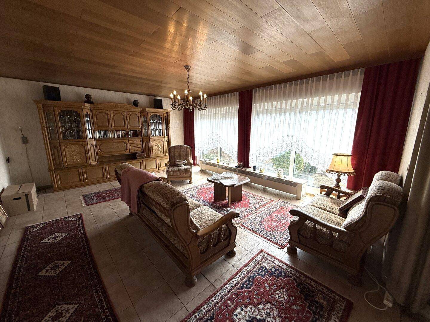 Wohnzimmer mit traditionellen Holzmöbeln, Fliesenboden und Blick ins Grüne, sehr gepflegt.