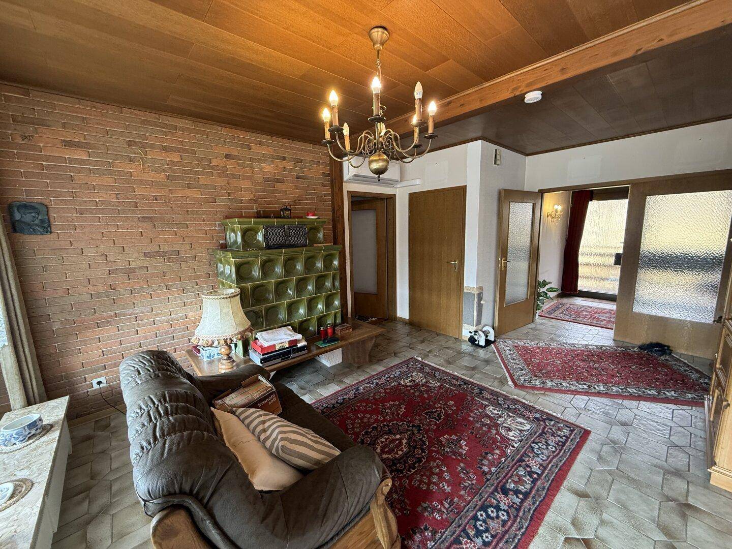 Geräumiges Wohnzimmer mit Kachelofen, Ziegelwand und traditionellem Mobiliar, sehr wohnlich.