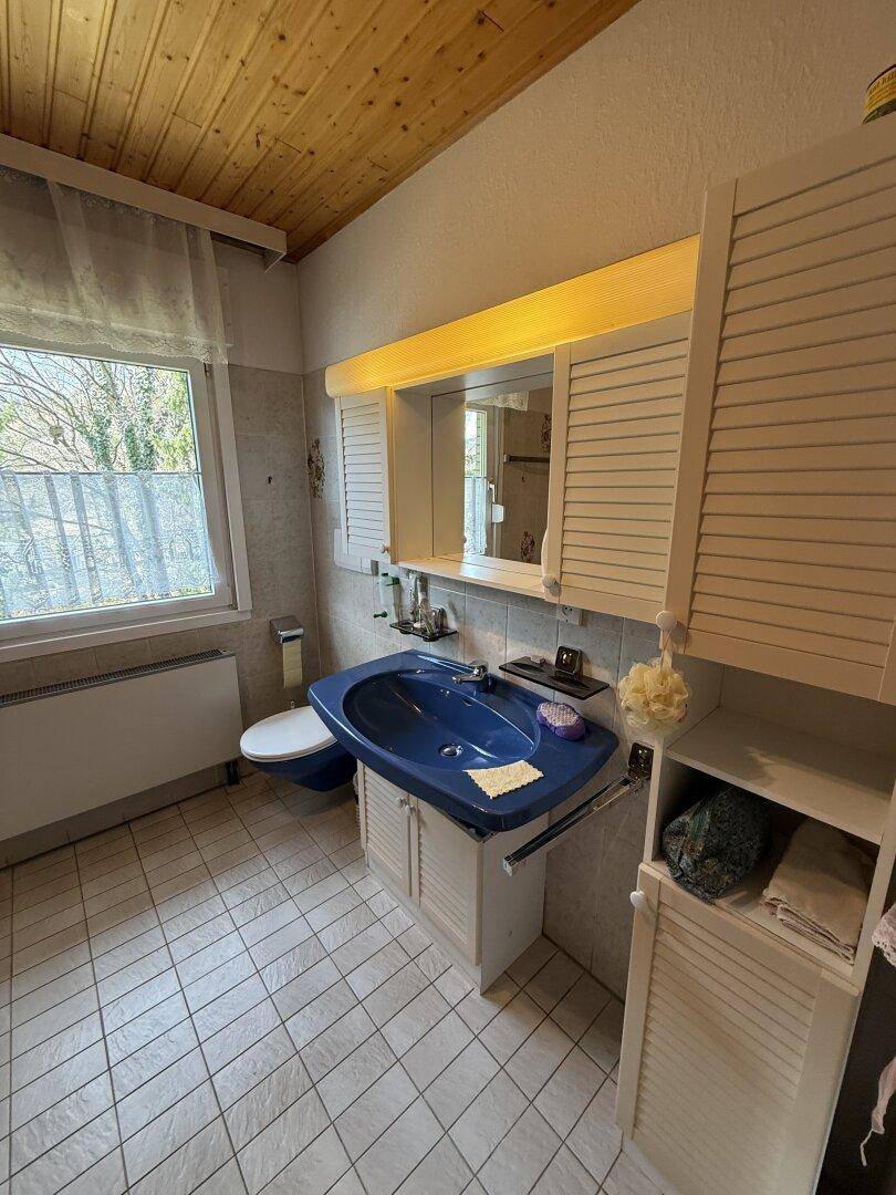 Badezimmer mit blauer Keramik, Fliesenboden und Fenster für Tageslicht, im Stil der 80er Jahre.