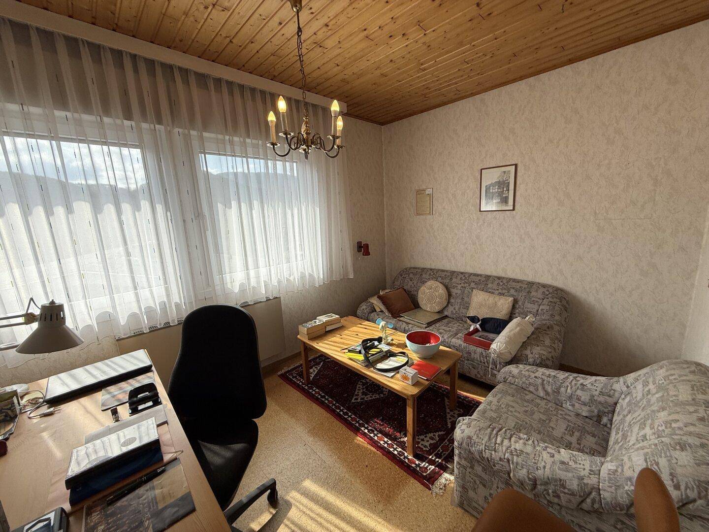 Arbeitszimmer mit Schreibtisch, Sofa und Fenster, das viel Licht hereinlässt, sehr funktional.