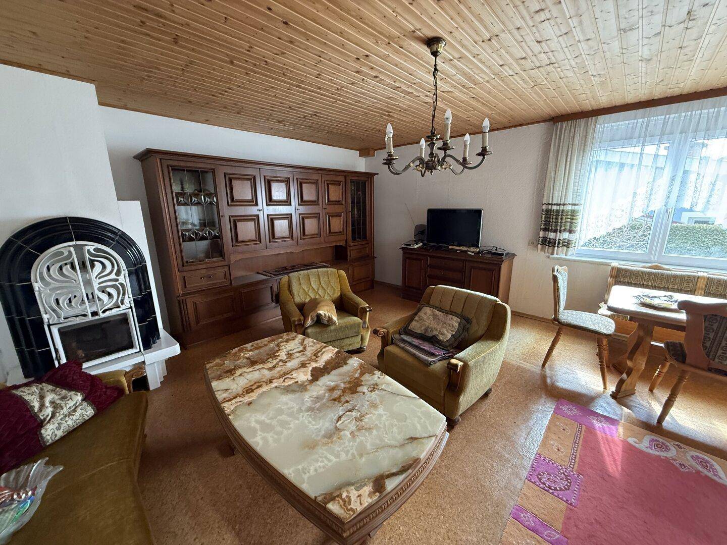 Wohnzimmer mit Kamin, Holzmöbeln und großem Fenster, das den Raum erhellt, sehr gemütlich.