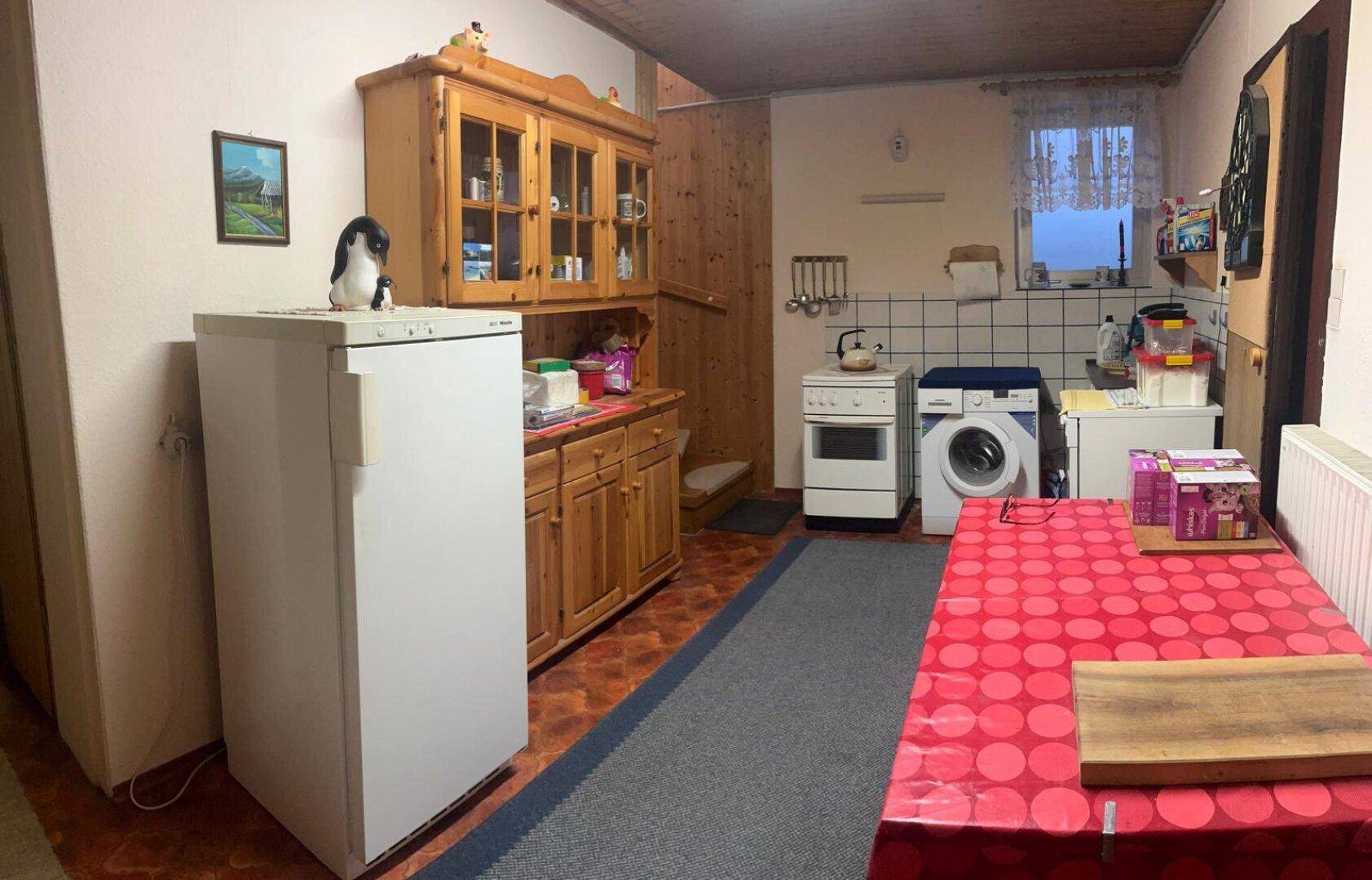 Einfache Küchenzeile mit Kühlschrank, Waschmaschine und Esstisch in einem Nebenraum, funktional.