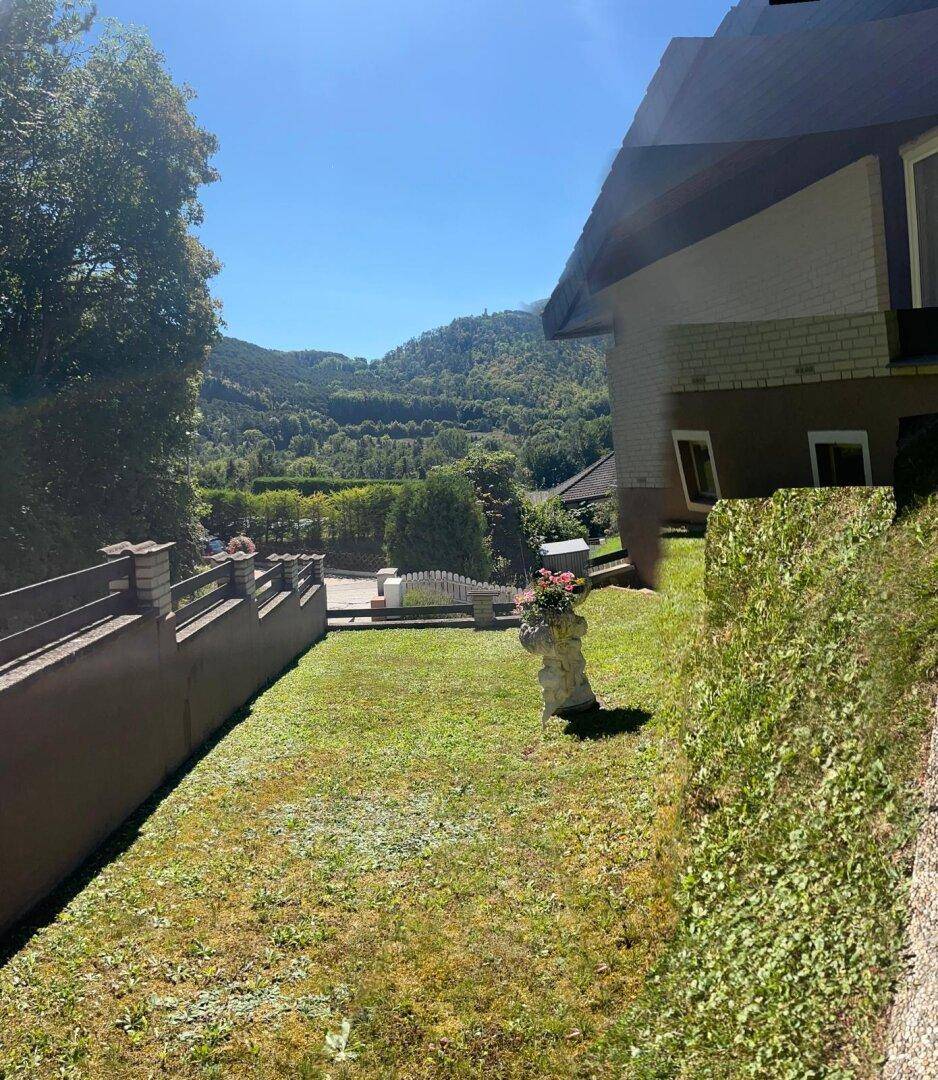 Sonniger Gartenbereich mit Rasenfläche und weitem Blick auf die bewaldeten Berge.
