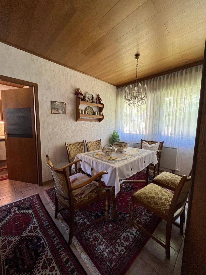 Esszimmer mit Holztisch, Stühlen und traditionellem Teppich, verbunden mit der Küche, sehr einladend.