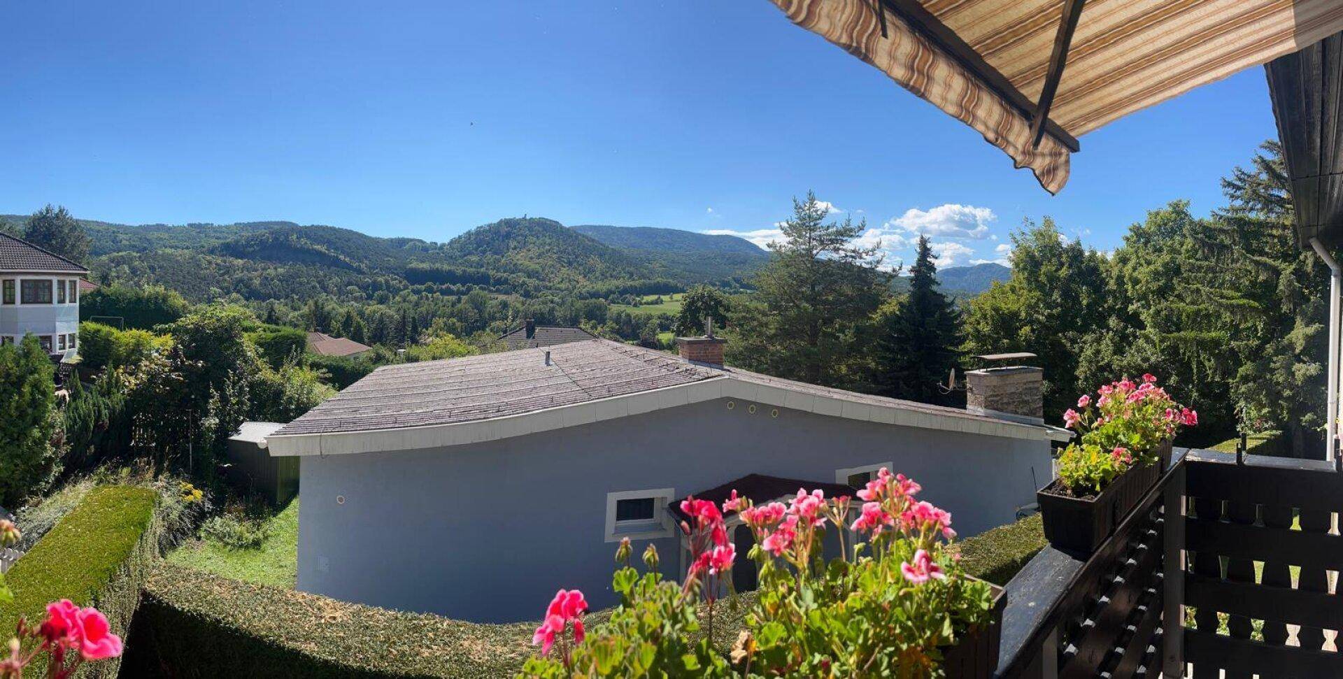 Panoramablick vom Balkon auf die weite, grüne Hügellandschaft unter blauem Himmel.