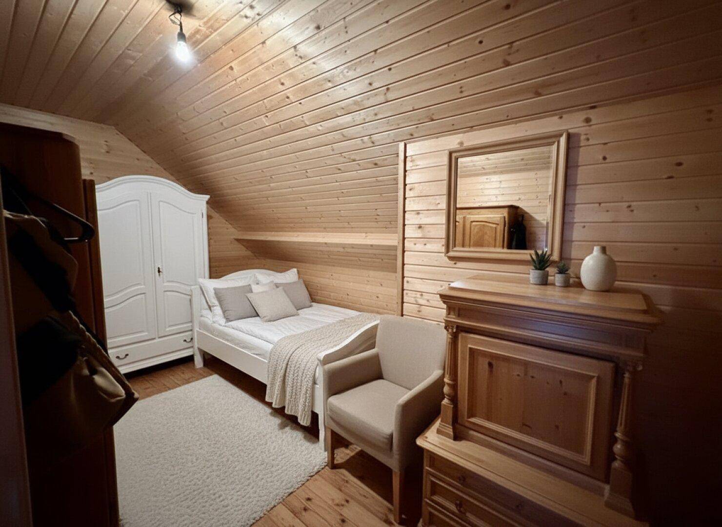Gemütliches Schlafzimmer im Dachgeschoss mit Holzvertäfelung, Einzelbett und natürlichem Lichteinfall.