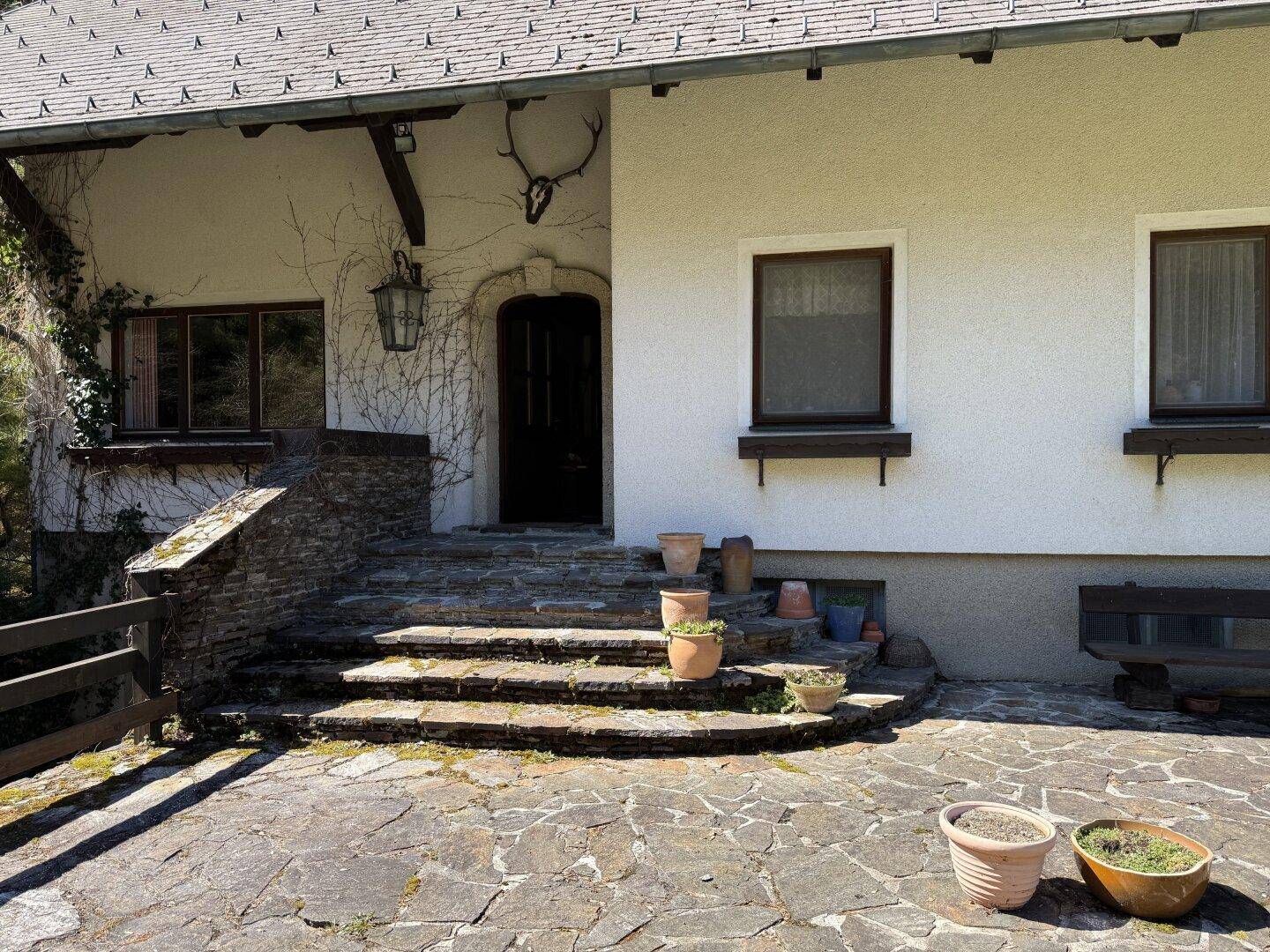 Nahaufnahme des Haupteingangs mit Steintreppe, Laterne und traditioneller Hirschgeweih-Dekoration.