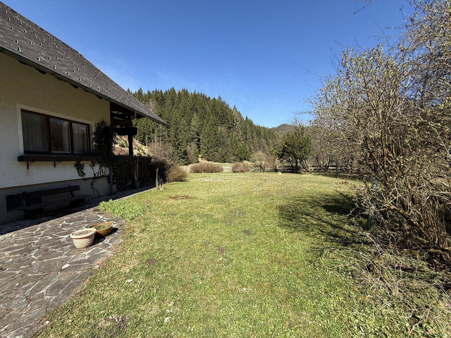 Weitläufiger Gartenbereich neben dem Haus mit Rasenfläche und Blick auf die umliegende Natur.
