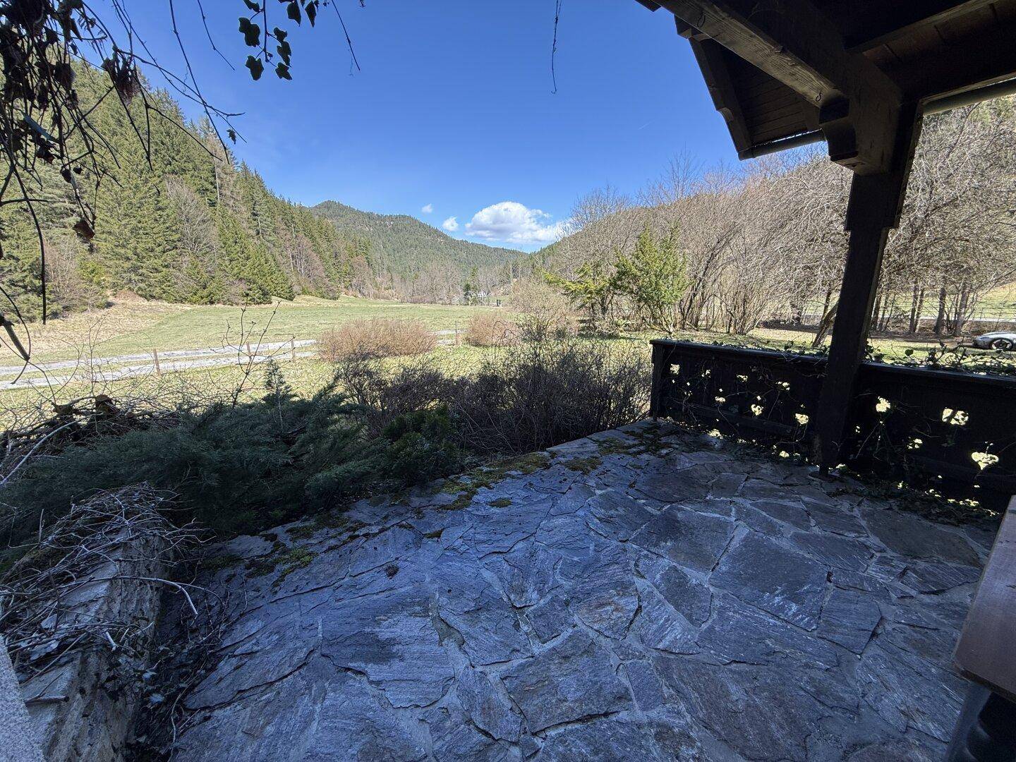 Überdachte Steinterrasse mit rustikalem Geländer und weitem Blick auf die grüne Landschaft.