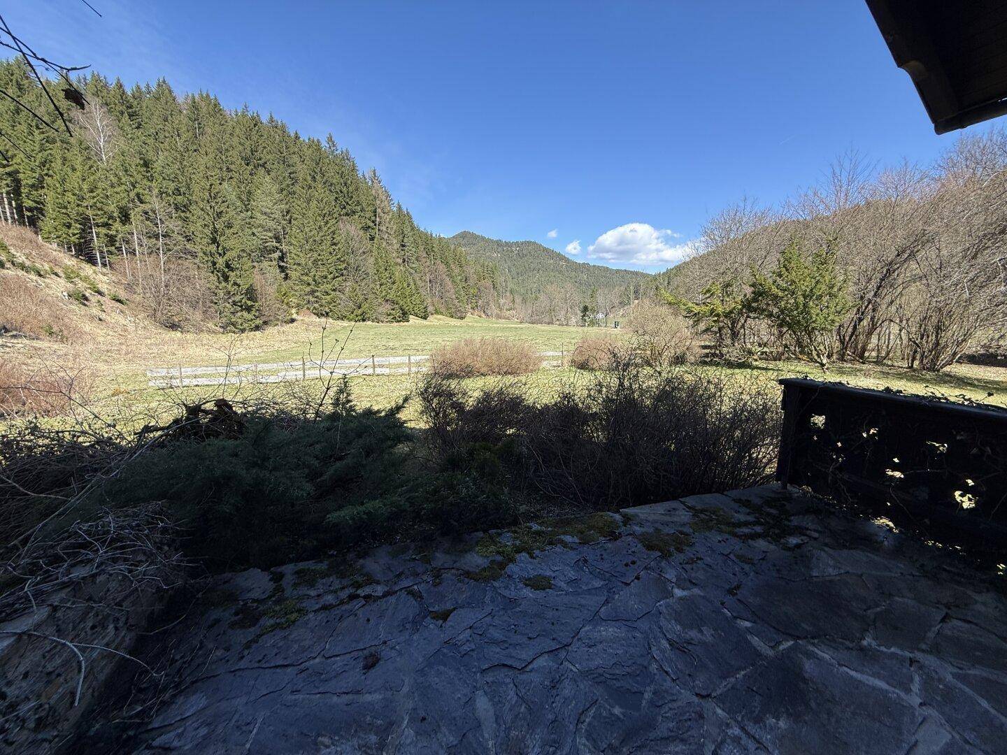 Rustikale Steinterrasse mit Holzbalken und Panoramablick auf die bewaldeten Hügel und das Tal.