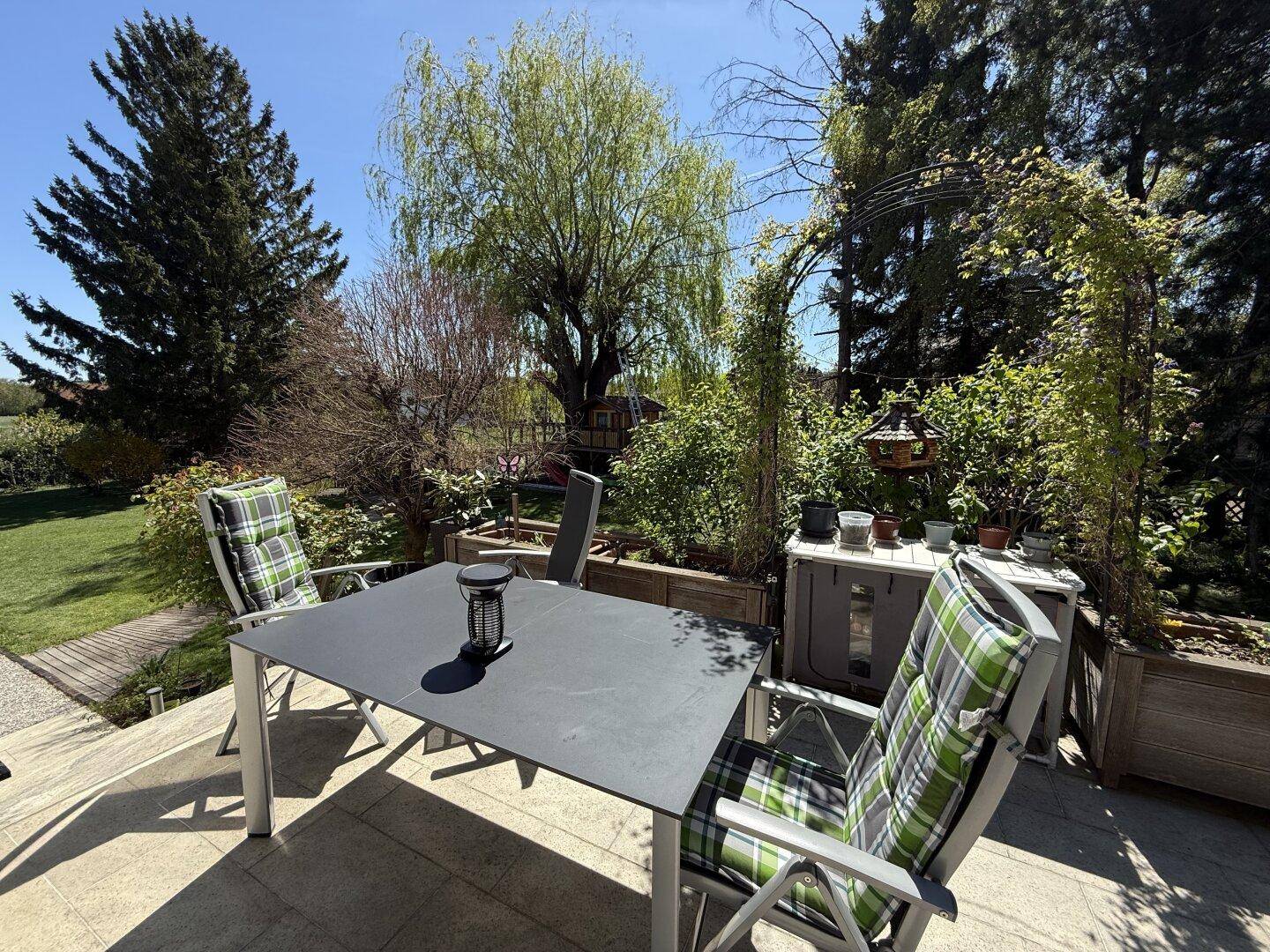 Einladende Terrasse mit Gartenmöbeln und Blick auf den gepflegten Garten mit Bäumen.