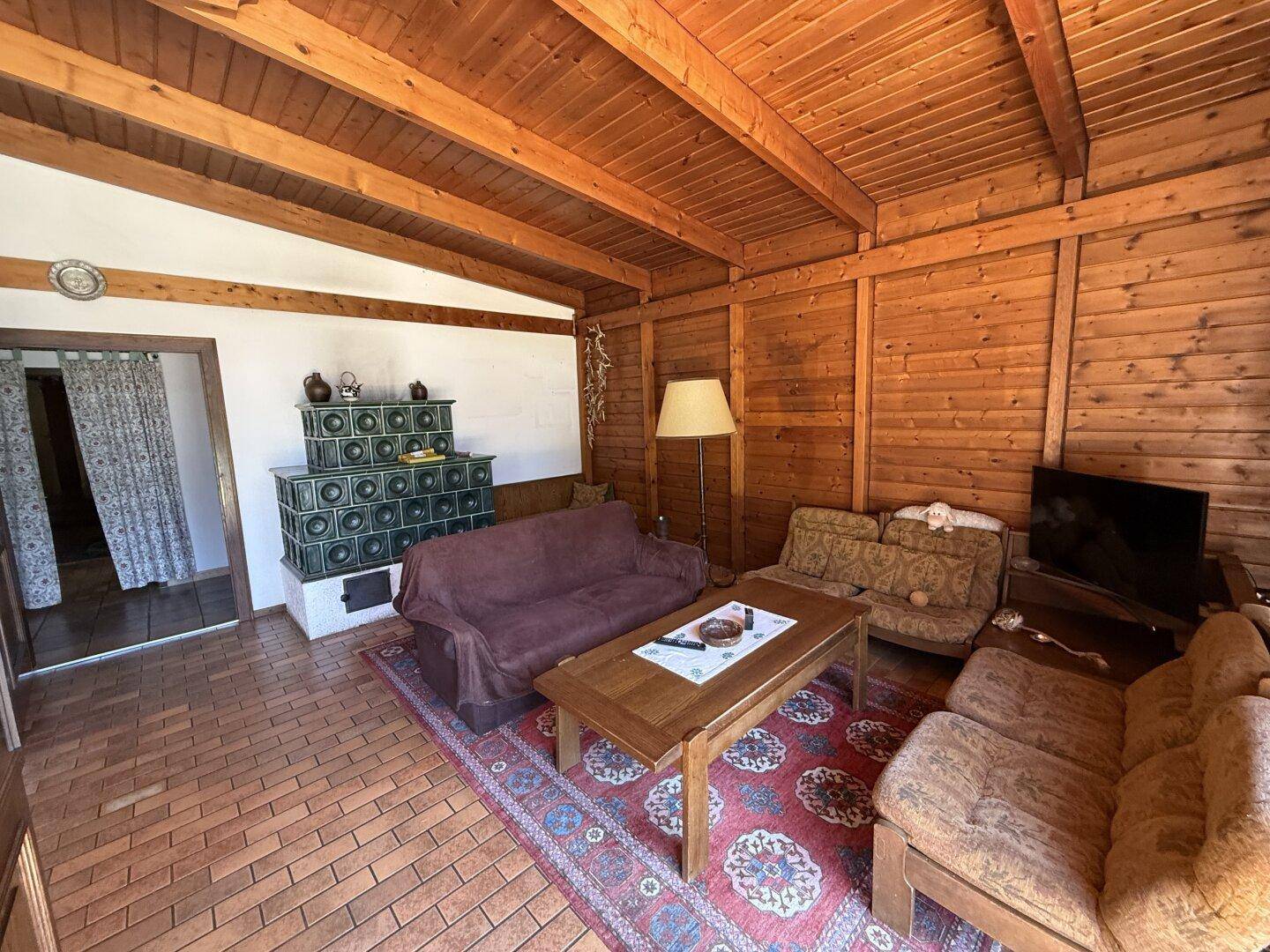 Rustikales Wohnzimmer mit Holzwänden, Kachelofen und traditioneller Einrichtung.