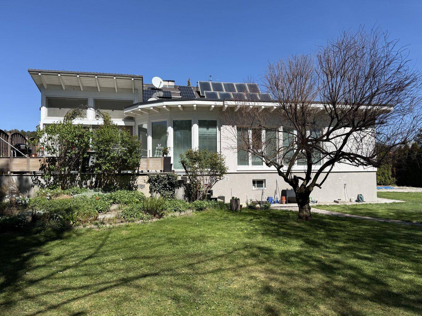 Rückansicht des Hauses mit großem Garten, Rasenfläche und Photovoltaikanlage auf dem Dach.