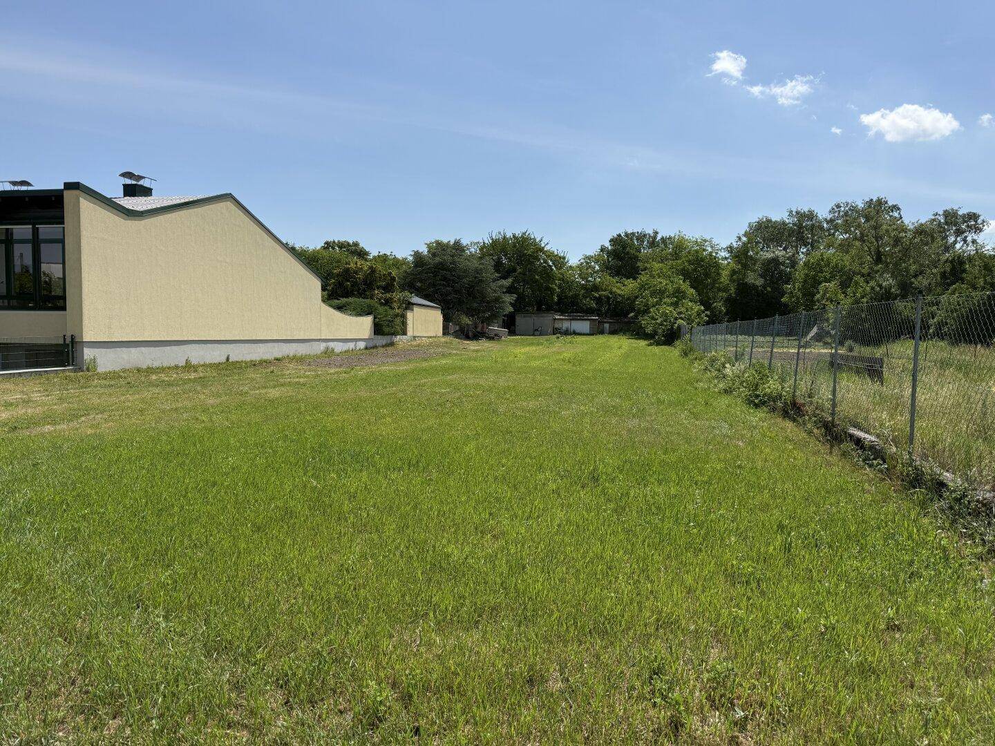 Weitläufiges grünes Grundstück mit angrenzendem Gebäude und dichter Vegetation im Hintergrund.