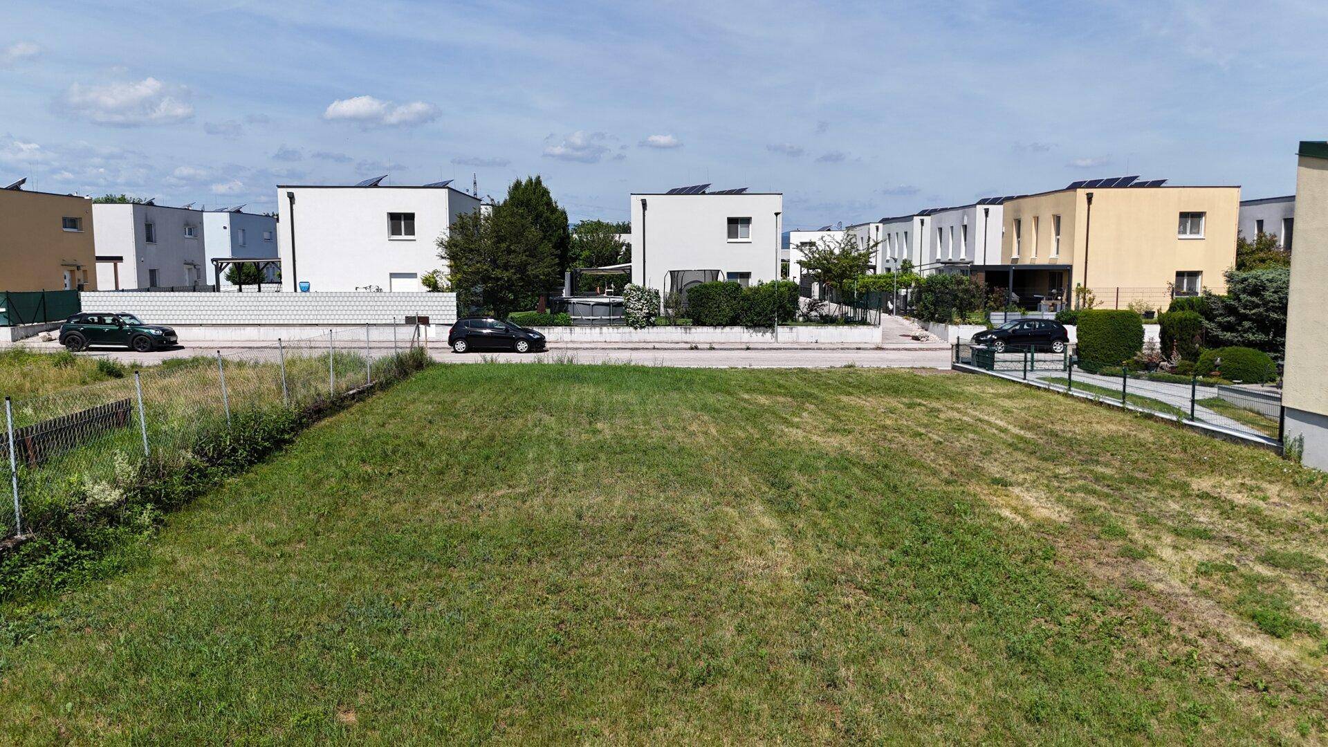 Luftaufnahme eines unbebauten Grundstücks umgeben von modernen Wohnhäusern mit Solaranlagen.