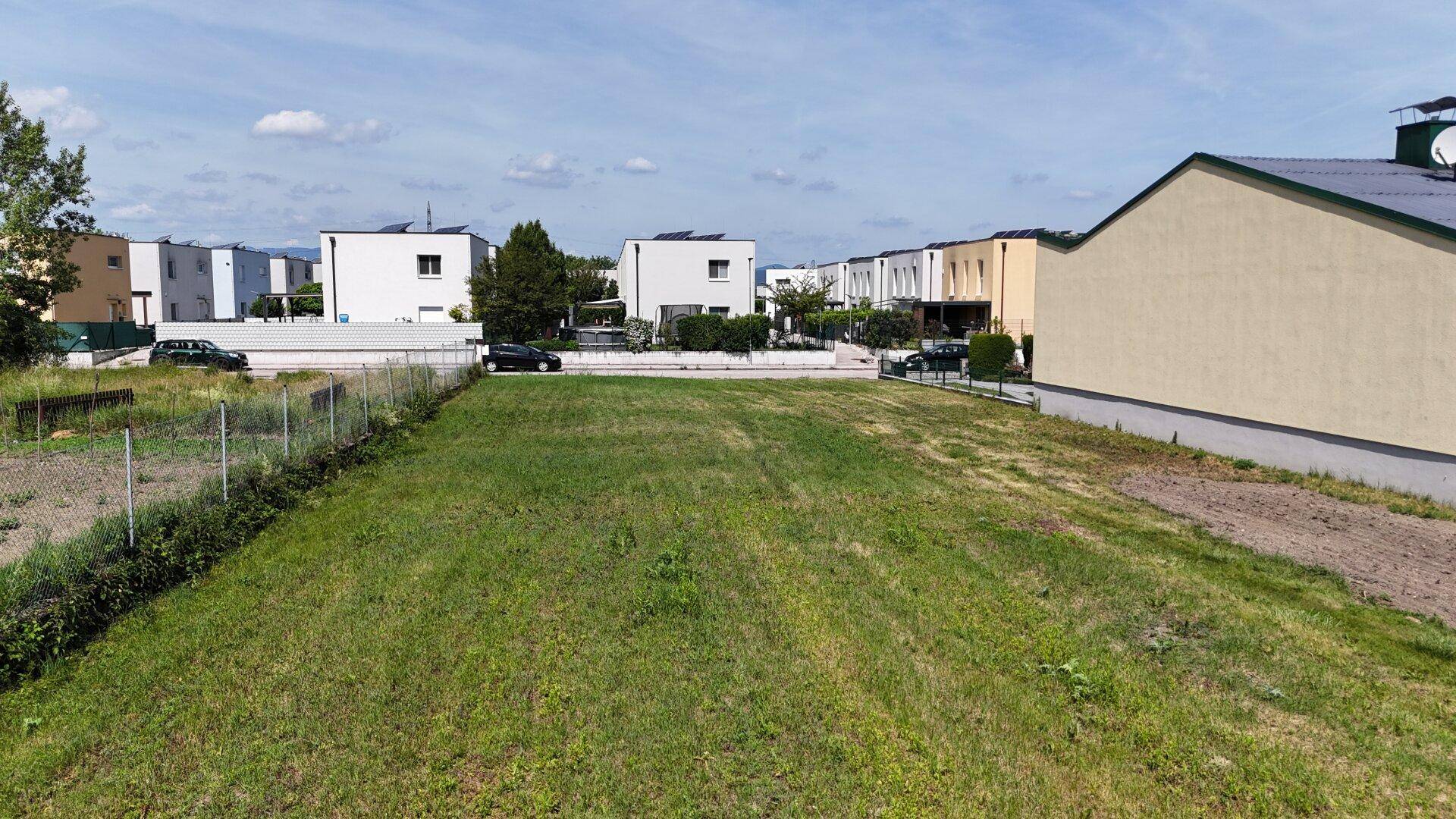 Luftaufnahme eines unbebauten Grundstücks umgeben von modernen Wohnhäusern mit Solaranlagen.