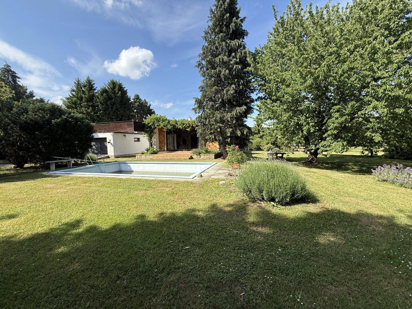 Weitläufiger Garten mit Pool und üppiger Vegetation, perfekt für sonnige Tage und Erholung.