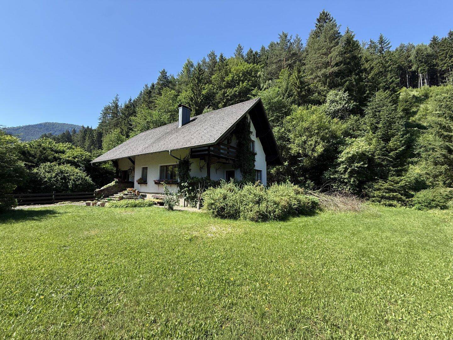 Idyllisches Haus in ländlicher Umgebung mit weitläufigem Rasen und bewaldeten Hügeln im Hintergrund.