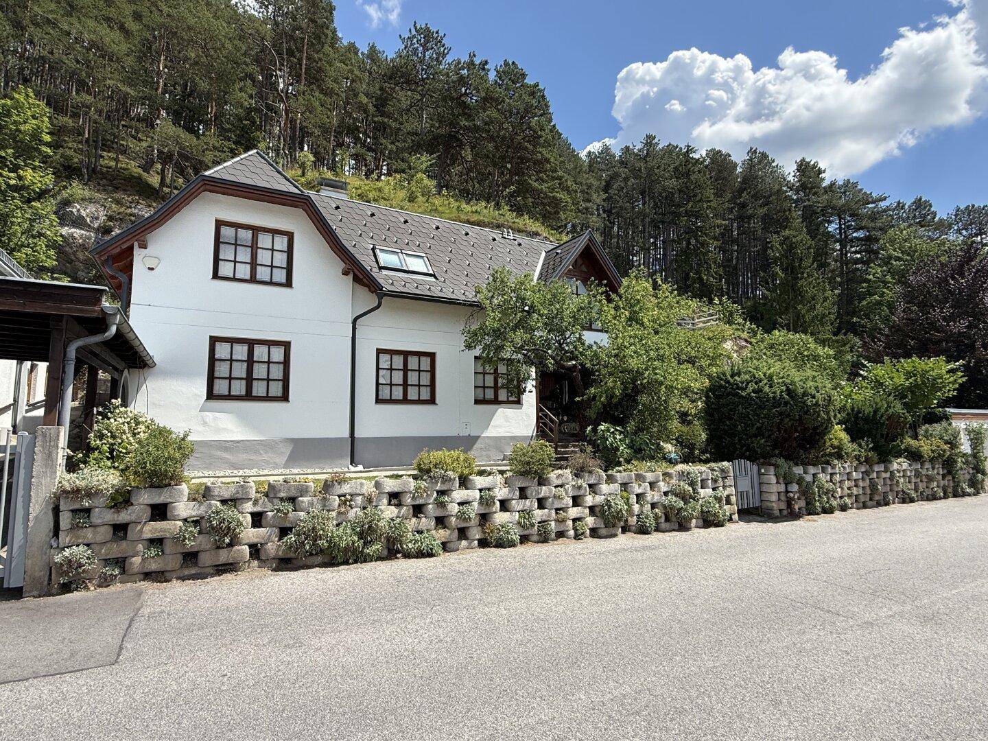 Weißes Einfamilienhaus mit traditionellen Fenstern und Blick auf die bewaldeten Hügel.