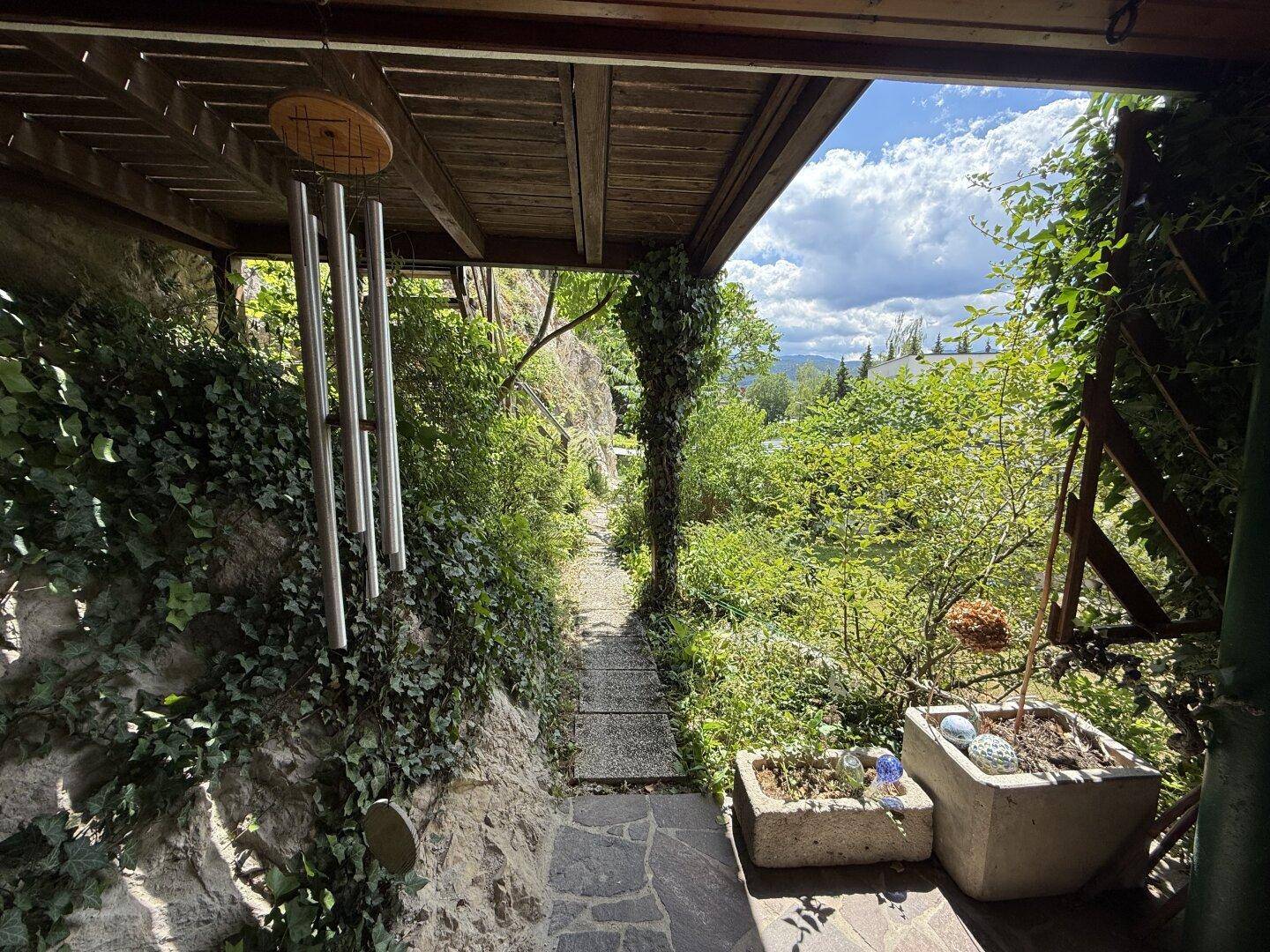 Verwunschener Gartenweg entlang einer bewachsenen Felswand mit üppiger Vegetation.