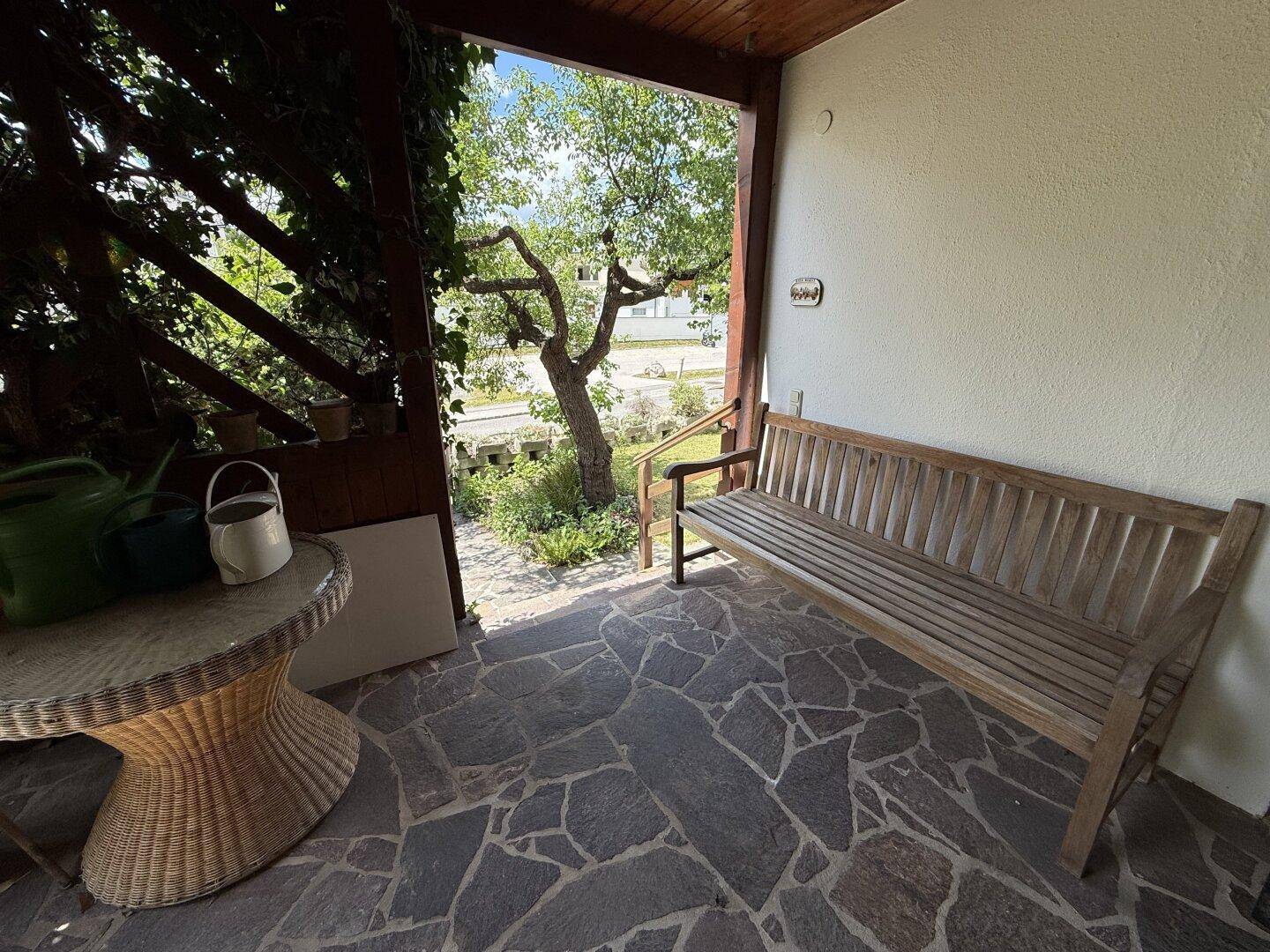 Überdachte Terrasse mit Steinboden und Holzbank, bietet einen ruhigen Sitzbereich im Freien.