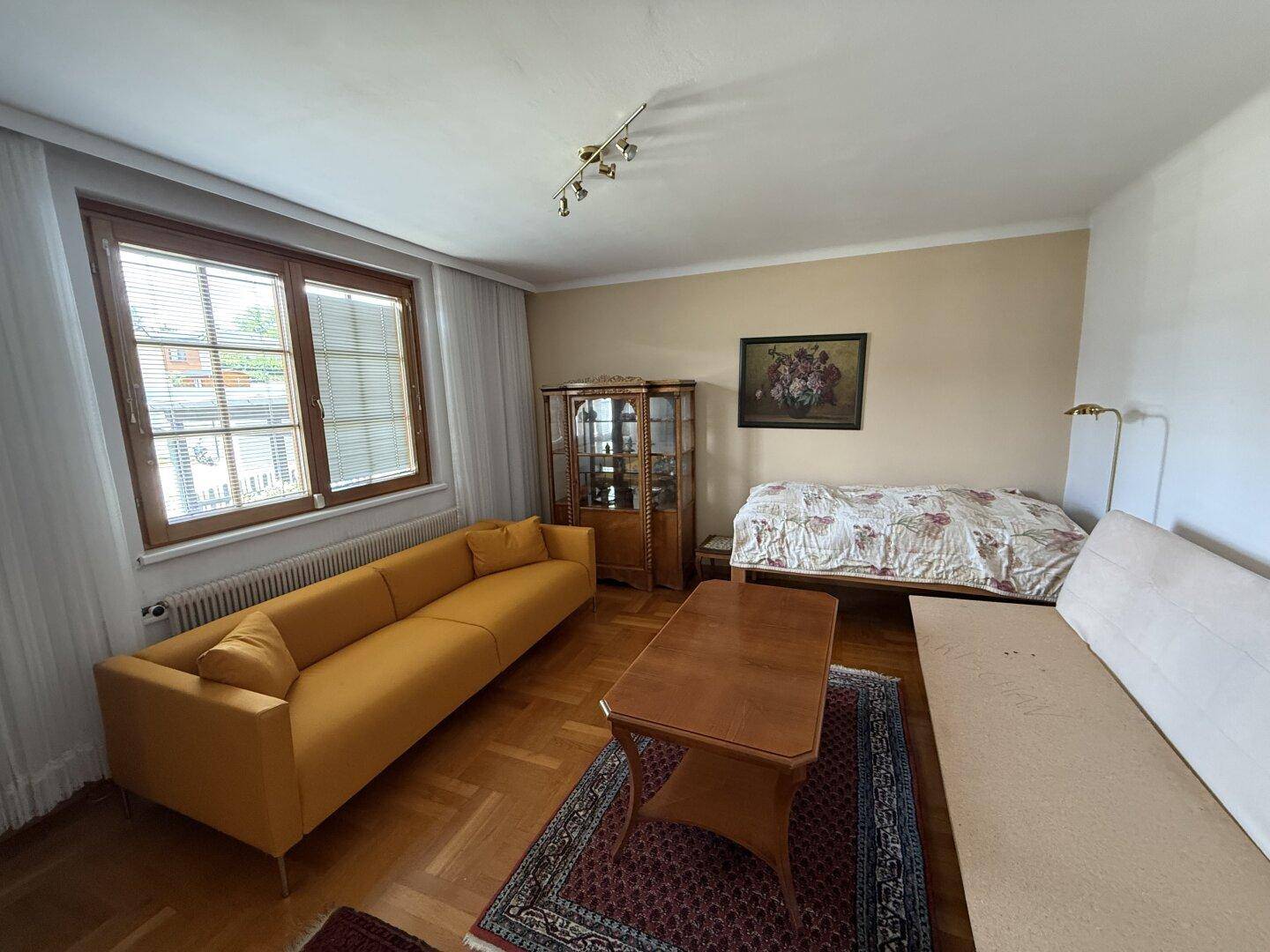 Helles Wohnzimmer mit gelbem Sofa, Holzboden und Blick ins Grüne durch das Fenster.