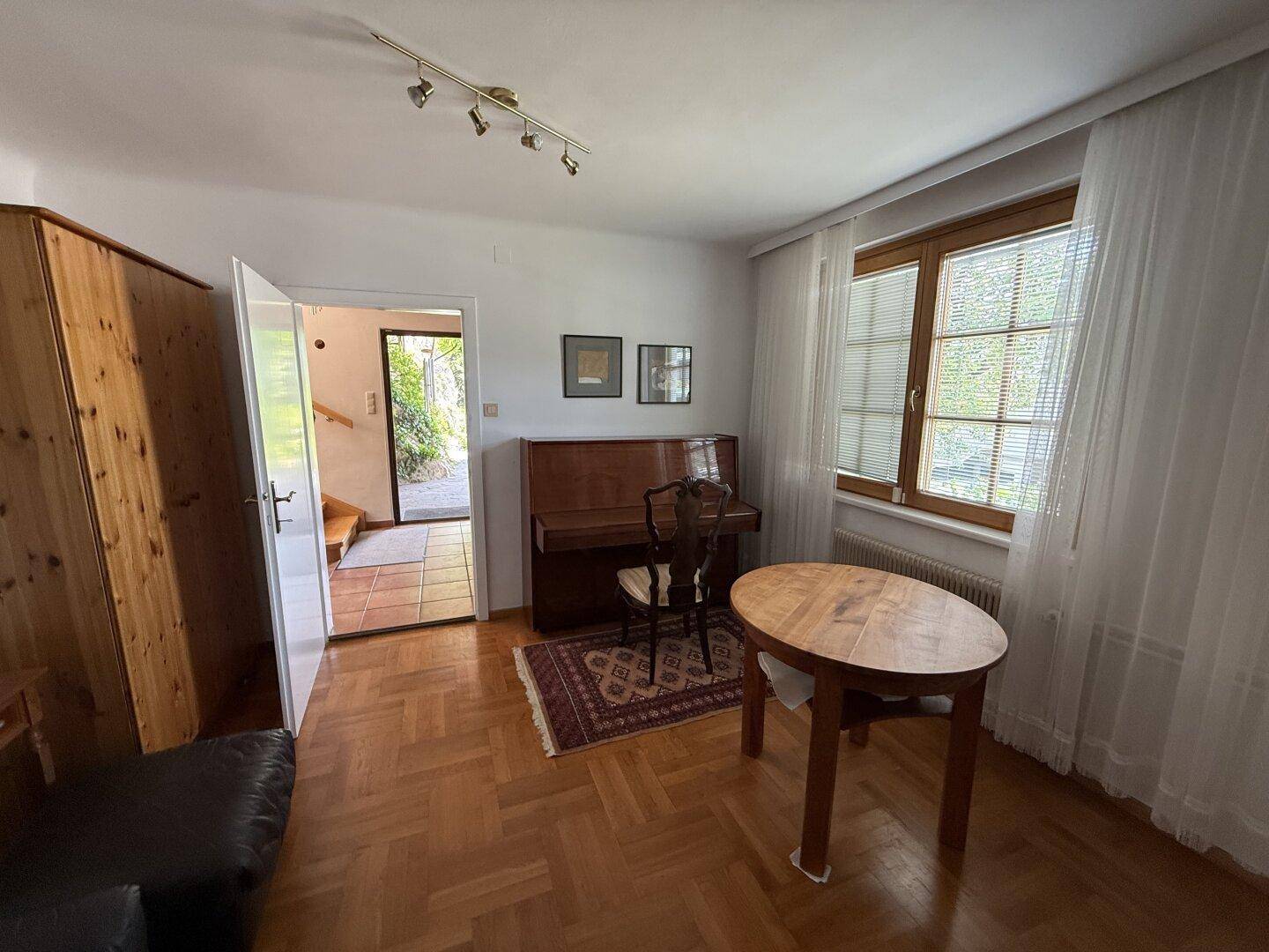 Heller Wohnbereich mit Klavier, Holzboden und Zugang zum Außenbereich.