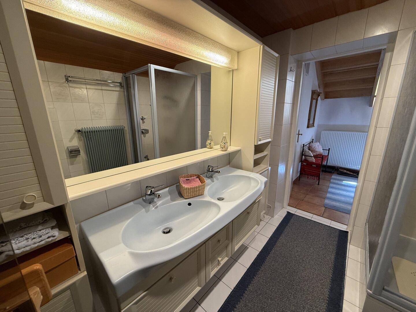 Badezimmer mit Doppelwaschbecken, Duschkabine und Fliesenboden in hellem Design.