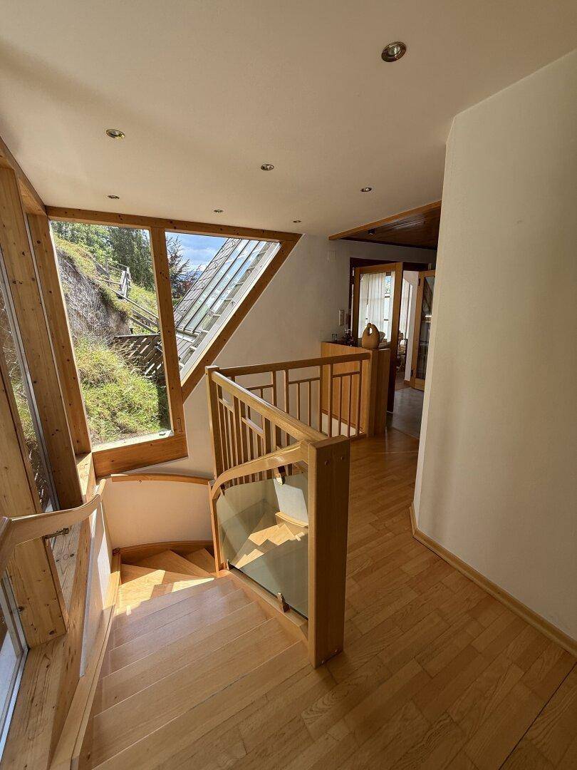 Heller Flur im Obergeschoss mit Holztreppe, Parkettboden und großen Fenstern.