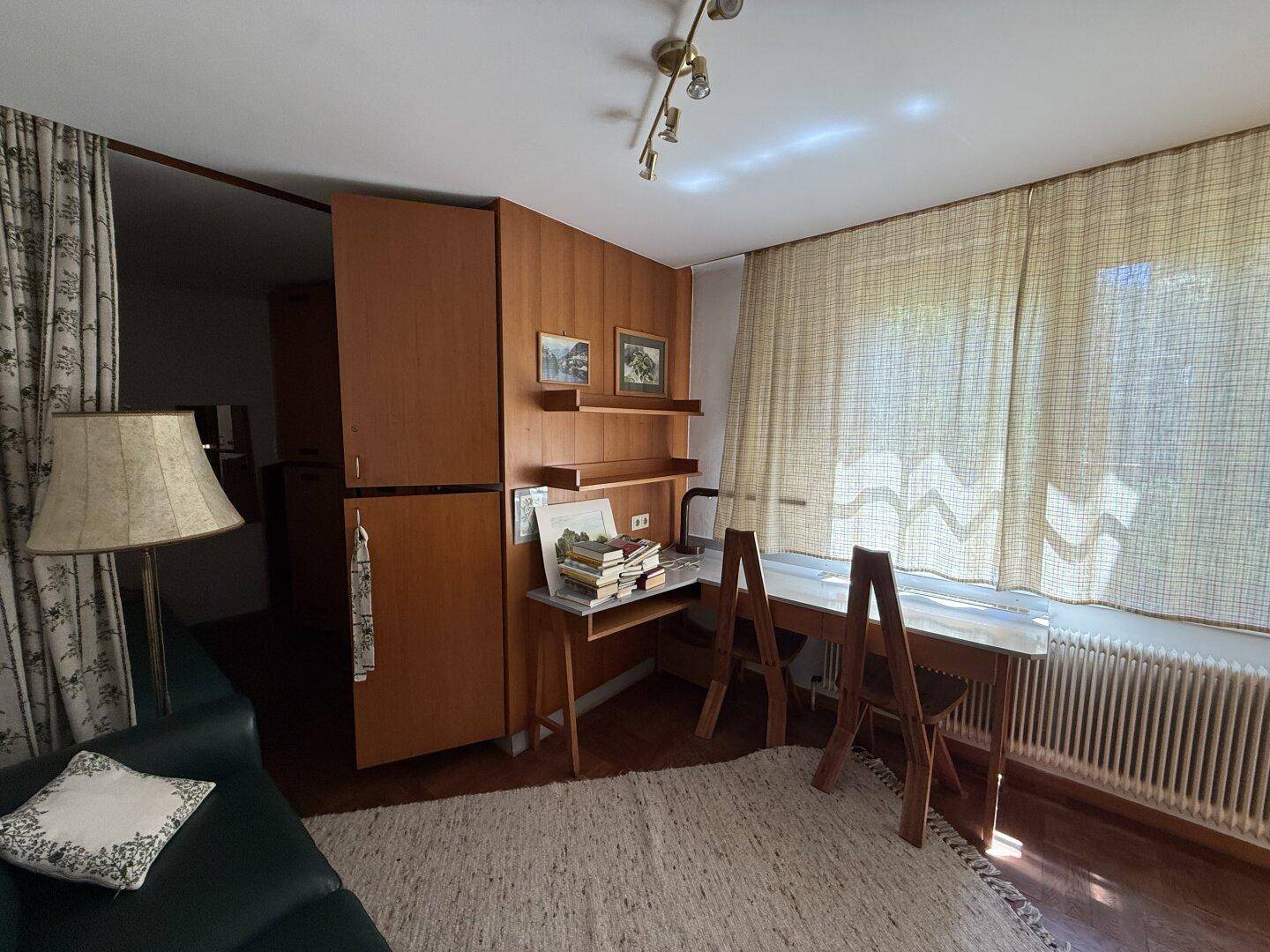 Arbeitszimmer mit Holzmöbeln, Schreibtisch und Blick ins Grüne durch das Fenster.
