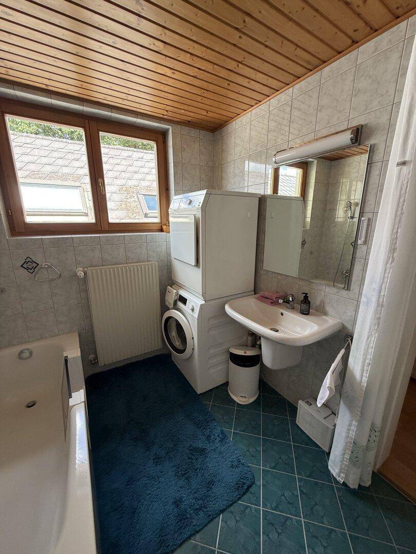 Badezimmer mit Badewanne, Waschmaschine und Trockner, sowie Holzdecke und Fliesenboden.