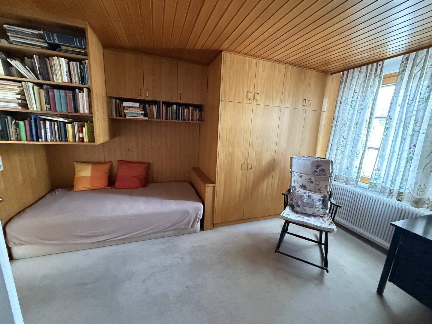 Schlafzimmer mit Holzwänden, Einbauschränken und einem Bett mit Bücherregal.