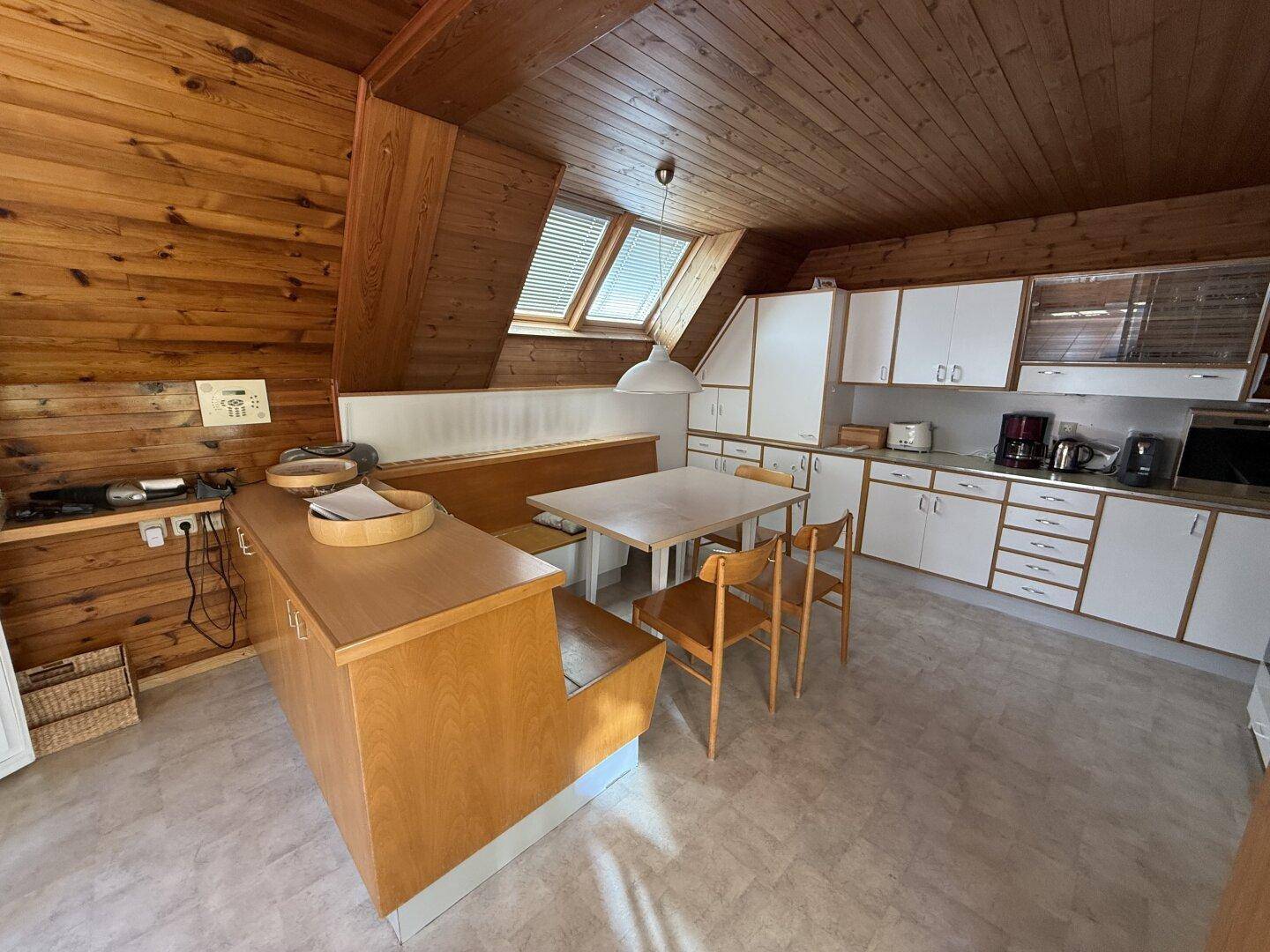 Rustikale Küche mit Holzdecke, Einbauküche und Essbereich unter Dachfenstern.