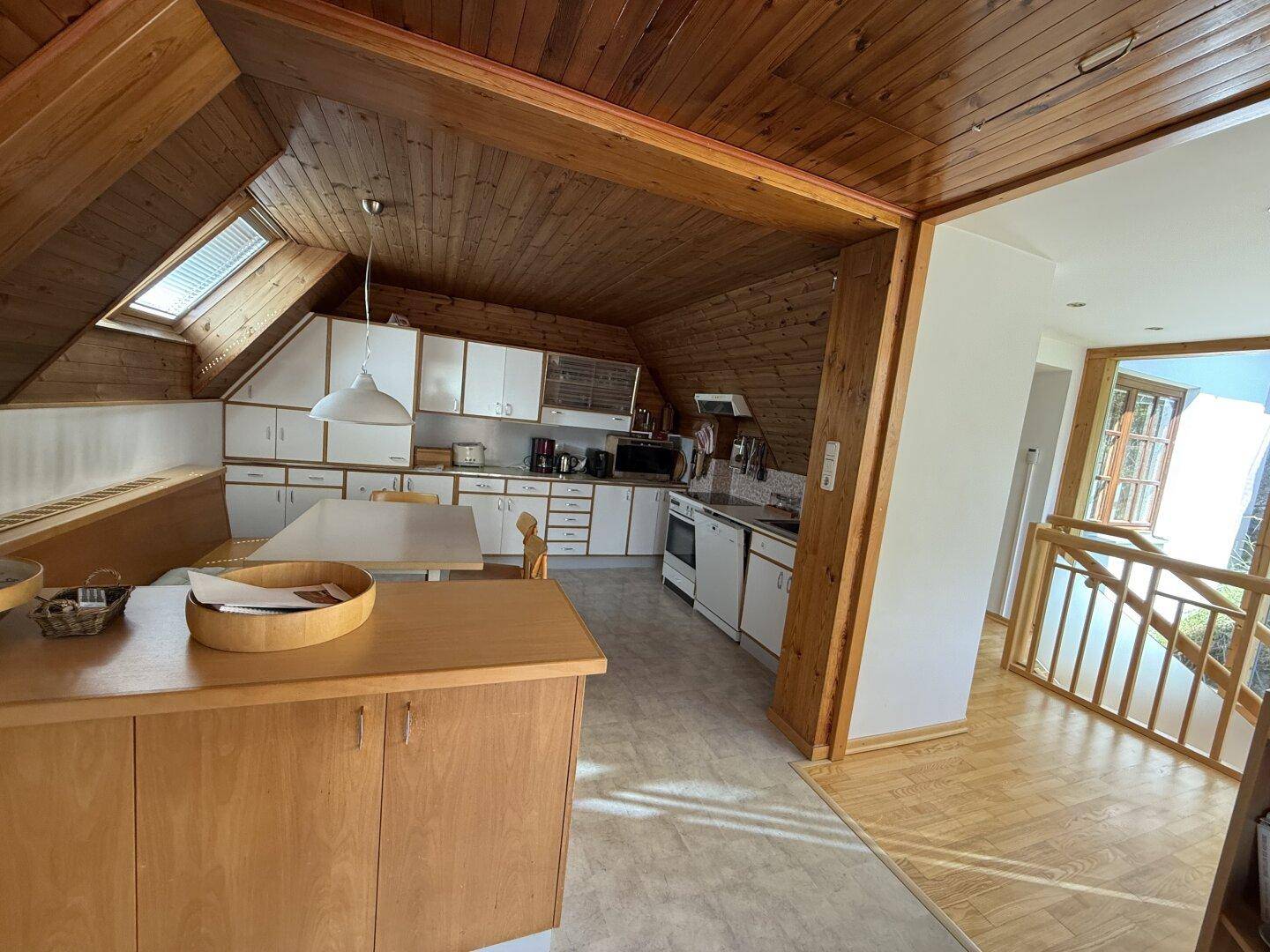 Geräumige Dachgeschossküche mit Holzbalken, Essbereich und Blick auf den angrenzenden Flur mit Treppe.