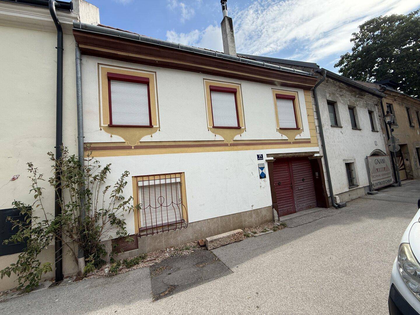 Ansicht der Hausfassade mit Fensterläden und einem großen Holztor an einer ruhigen Straße.