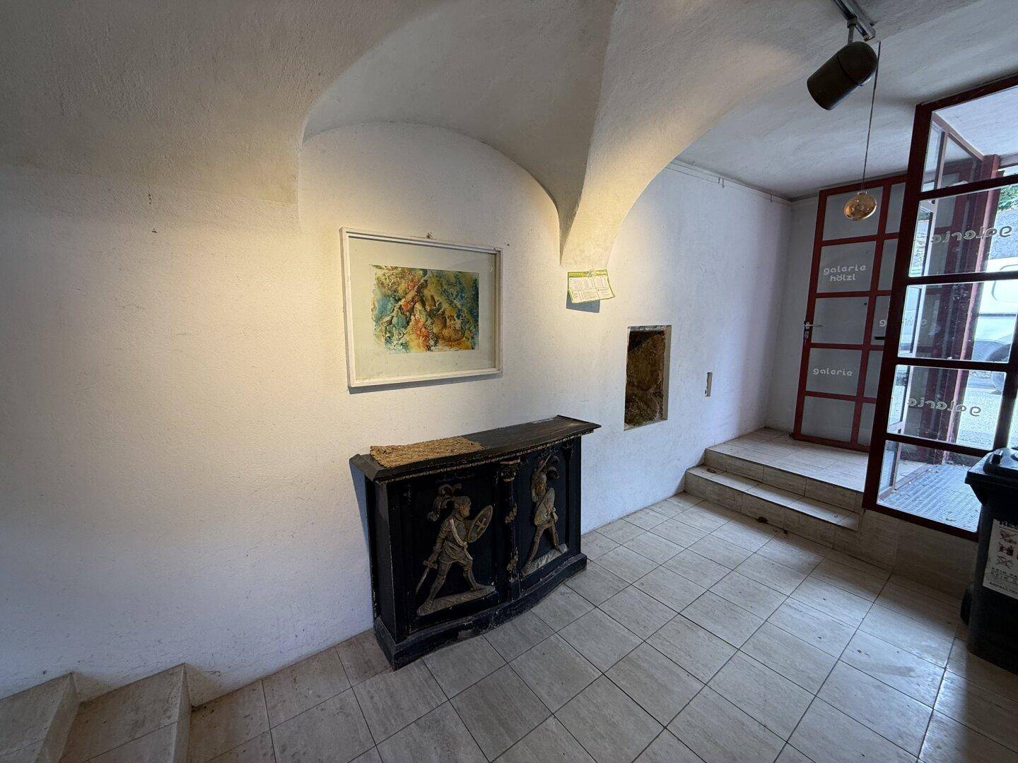 Gewölbter Eingangsbereich mit Fliesenboden, Kunstwerken und einem antiken Möbelstück.