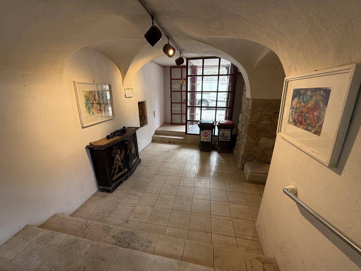 Gewölbter Flur mit Fliesenboden, Kunstwerken und Treppe zu den oberen Etagen.