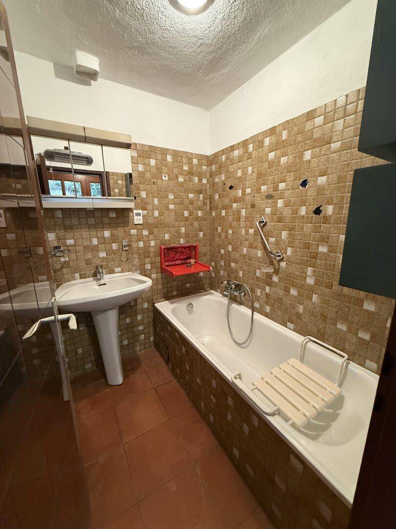 Badezimmer mit Badewanne, Waschbecken und braunen Fliesen im Retro-Stil.