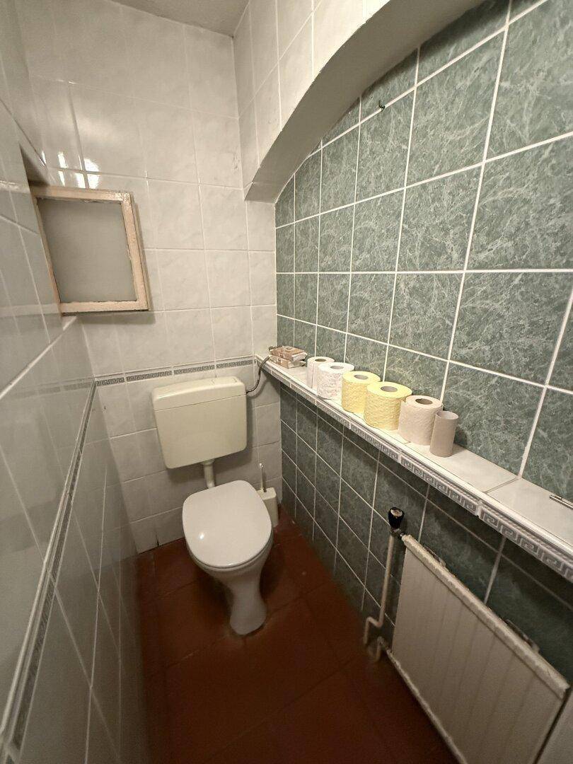Separate Toilette mit grünen Fliesen, Fenster und Heizkörper.